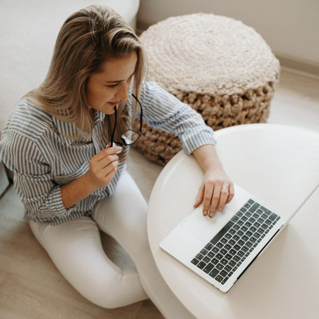 Smiling woman holding glasses while working on a laptop, representing a creative entrepreneur setting up a client questionnaire